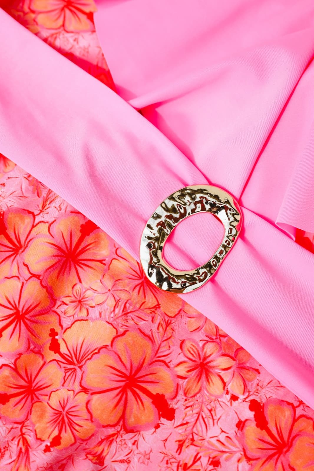 Detalhe do padrão Hibiscus: flores laranja sobre rosa, com uma fivela dourada